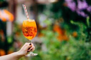 cocktail fresco in bicchiere di vino all'aperto su sfondo sfocato. la donna tiene una bevanda fredda estiva con ghiaccio. tiro orizzontale. gustosa bevanda alcolica foto