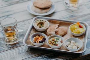 immagine aerea del cibo tradizionale israeliano sul vassoio. hummus, formaggio di capra domestico, torsolo di pomodoro, barbabietola con spezie, pane pita, bevanda in vetro foto