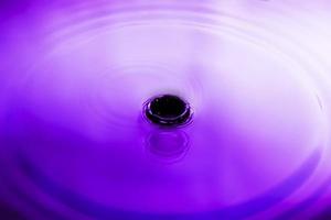 acqua spruzzata viola astratta la superficie dell'acqua si diffonde in cerchi scintillanti. foto