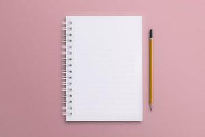 un quaderno bianco e una matita posizionati su una superficie di carta rosa. foto