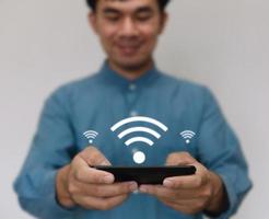 il giovane bello che indossa una camicia azzurra usa lo smartphone connesso alla tecnologia wi-fi per utilizzare la funzione casa intelligente. business tecnologico e concetto di stile di vita moderno. foto