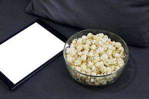 tazza di vetro con tavoletta digitale popcorn salato in una poltrona grigia. foto