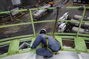 lavoratore di sesso maschile che indossa la prima imbracatura di sicurezza e solitario di sicurezza che lavora in alto posto sul corrimano sul serbatoio del tetto superiore. foto