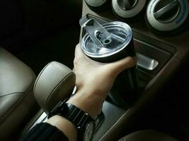 la mano di una donna sta raccogliendo una tazza termica in acciaio inossidabile nera posta nell'auto. foto