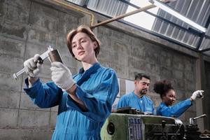 la giovane operaia caucasica dell'industria lavora con strumenti di precisione per la lavorazione dei metalli, macchine per tornio e officina di pezzi di ricambio con un team multirazziale nella fabbrica di produzione, ingegneri meccanici professionisti. foto