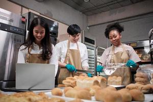 tre giovani amici e partner di avvio di pasta per il pane e pasticcini impegnati con lavori di pasticceria fatti in casa mentre cucinano ordini online, imballano e consegnano in panetteria, piccolo imprenditore foto