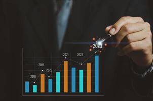 analisi delle tendenze di crescita del business e delle finanze aziendali uomo d'affari che lavora con grafico e grafico a schermo virtuale. freccia che punta al 2023 foto