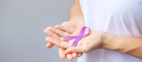 mano che tiene il nastro viola per il mese di sensibilizzazione del pancreas, dell'esofago, del testicolo, dell'alzheimer mondiale, dell'epilessia, del lupus, della sarcoidosi, della fibromialgia e della violenza domestica. concetto di giornata mondiale del cancro foto