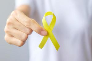 mano che tiene un nastro giallo per sostenere le persone che vivono e le malattie. settembre giorno di prevenzione del suicidio, infanzia, sarcoma e concetto di mese di consapevolezza del cancro alle ossa foto