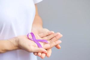 mano che tiene il nastro viola per il mese di sensibilizzazione del pancreas, dell'esofago, del testicolo, dell'alzheimer mondiale, dell'epilessia, del lupus, della sarcoidosi, della fibromialgia e della violenza domestica. concetto di giornata mondiale del cancro foto