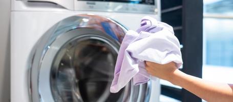 casalinga donna mano che tiene i vestiti all'interno della lavatrice in lavanderia foto