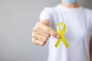 mano che tiene un nastro giallo per sostenere le persone che vivono e le malattie. settembre giorno di prevenzione del suicidio, infanzia, sarcoma e concetto di mese di consapevolezza del cancro alle ossa foto