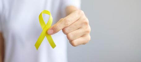 mano che tiene un nastro giallo per sostenere le persone che vivono e le malattie. settembre giorno di prevenzione del suicidio, infanzia, sarcoma e concetto di mese di consapevolezza del cancro alle ossa foto