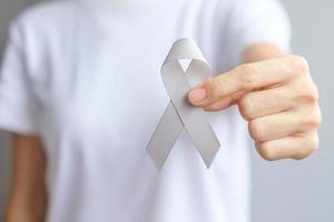 mese di sensibilizzazione sul cancro al cervello, mano di donna che tiene un nastro di colore grigio per sostenere le persone che vivono. concetto di salute e giornata mondiale del cancro foto