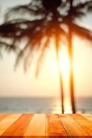 tavola di legno con mare sfocato e sfondo di albero di cocco al tramonto. concetto di spiaggia in estate. foto