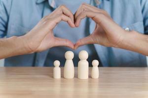 le mani dell'uomo che fanno a forma di cuore su bambole di legno. pianificazione, salvataggio della famiglia, assistenza sanitaria e assicurazioni, salute mentale della famiglia, giornata internazionale delle famiglie foto