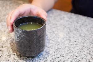 tazza di tè verde caldo della stretta della mano della donna foto