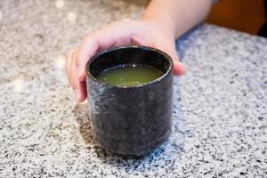 tazza di tè verde caldo della stretta della mano della donna foto