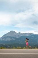 una ragazza corre lungo una strada asfaltata sullo sfondo di bellissime montagne foto