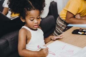 i bambini della figlia prescolare nera americana che fanno i compiti imparano l'educazione con sua sorella che vivono insieme a casa. foto
