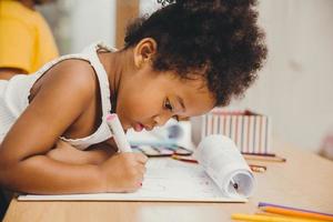 primo piano piccolo bambino ragazza pelle nera che scrive facendo i compiti a casa. foto