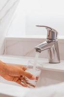 uomo che riempie un bicchiere d'acqua al lavandino in bagno. foto