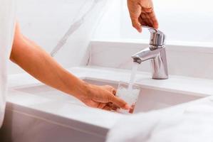 uomo che riempie un bicchiere d'acqua al lavandino in bagno. foto