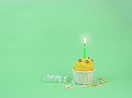 Cupcake giallo dolce con candela di prua su sfondo verde con spazio per la copia. concetto di sfondo festa di buon compleanno. foto
