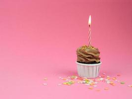 Cupcake al caffè dolce con candela a fiocco su sfondo rosa con spazio per la copia. concetto di sfondo festa di buon compleanno. foto