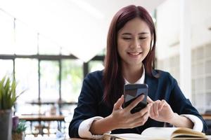 donna asiatica che parla al telefono e lavora su un laptop con una faccia sorridente, conversazioni telefoniche aziendali, lavoro al bar, stile di vita del bar, soggiorno al bar, nuova normalità, apprendimento, distanza sociale. foto