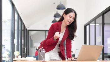 donna felice eccitata che guarda lo schermo del telefono, celebrando una vittoria online, giovane donna asiatica felicissima che urla di gioia in ufficio foto