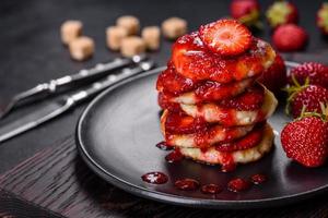 frittelle di ricotta con fragole a fette e marmellata di fragole su un piatto su uno sfondo di cemento foto