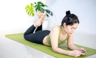 donne che giocano al cellulare e si siedono sul tappetino da yoga verde mentre riposano per una pratica in casa. foto