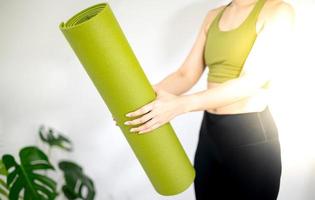 mano femminile che tiene tappetino yoga verde per preparare l'esercizio sul tappetino. foto