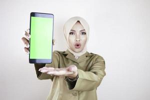 donna asiatica scioccata che indossa l'uniforme marrone che punta il dito sullo schermo verde sullo smartphone in mano foto