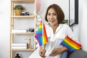 ragazza asiatica che tiene la bandiera arcobaleno lgbtq nella sua camera da letto per uscire dall'armadio e celebrare il mese dell'orgoglio per promuovere la diversità sessuale e l'uguaglianza nel concetto di orientamento omosessuale foto