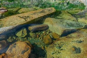 grandi blocchi di granito e molte piccole pietre giacciono sotto l'acqua limpida e limpida sul fondo del lago foto