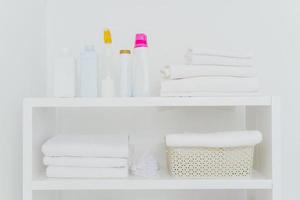 lavanderia con asciugamani ben piegati, bottiglie di detersivo liquido o detersivi. tutto nei colori bianco. faccende quotidiane e giornata di lavanderia foto