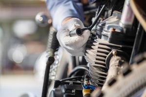 controllo meccanico della candela del motociclo nel garage dell'officina, uomo che ripara la moto in officina, concetti di riparazione e manutenzione foto