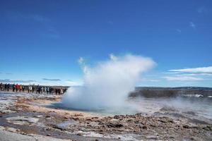 turisti che guardano l'eruzione del geyser di Strokkur nella valle contro il cielo blu foto