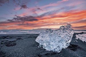 bellissimo cristallo di ghiaccio sulla sabbia nera della spiaggia di diamante contro il cielo nuvoloso al tramonto foto