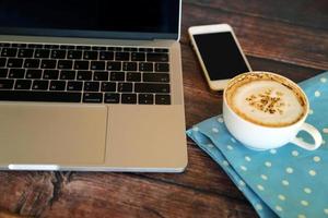 laptop con smartphone e caffè caldo su un tavolo di legno, funzionante in remoto. foto