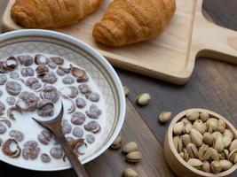 primo piano di cereali per la colazione con latte, croissant e pistacchi su fondo di legno. foto