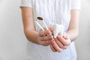 concetto di cure odontoiatriche. mano della donna che tiene il modello di dente sano bianco e gli strumenti del dentista dentale isolati su sfondo bianco. sbiancamento dei denti, igiene orale dentale, restauro dei denti, giornata del dentista. foto