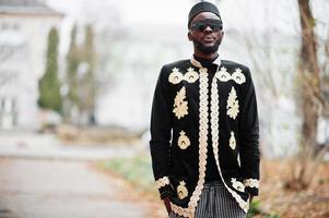 mega uomo africano alla moda nella tradizionale posa della giacca. ragazzo nero alla moda con cappello e occhiali da sole. foto