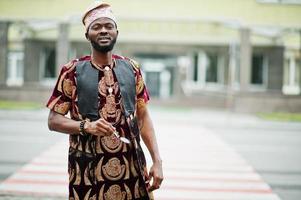 uomo africano elegante e bello in abito tradizionale e berretto in piedi all'aperto. foto