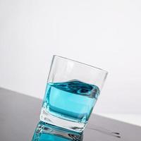 bicchiere per liquore mettere liquido blu in vetro appoggiato su un tavolo inclinato sfondo bianco foto