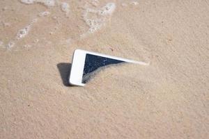 telefono cellulare bianco sulla sabbia al concetto di spiaggia rifiuti elettronici foto