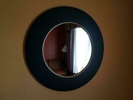 Specchio circolare nero dell'hotel sulla parete con finestra e sedia foto