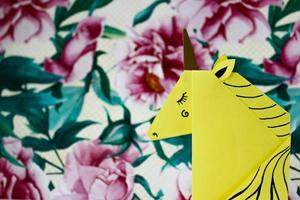 unicorno giallo realizzato con la tecnica dell'origami sul lato destro della foto su sfondo floreale.